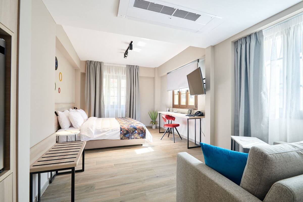 A modern hotel room with a bed, a desk, a chair, and a sofa.