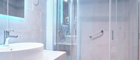 Un baño moderno con ducha envuelta en vidrio, un lavabo redondo y un perchero para toallas.