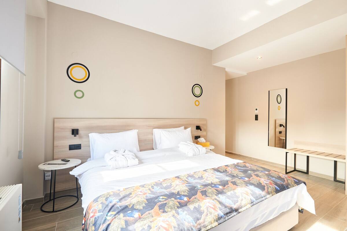 A modern hotel room with a large bed, bedside tables, a round mirror, and a small side table.