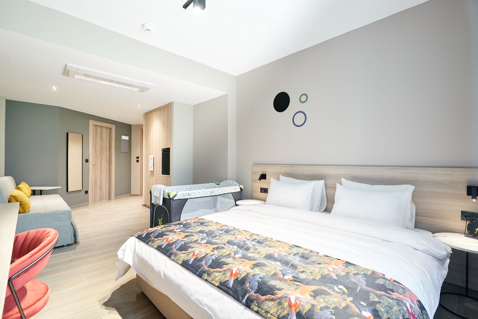A modern hotel room with a large bed, a small desk, a chair, and a wardrobe.