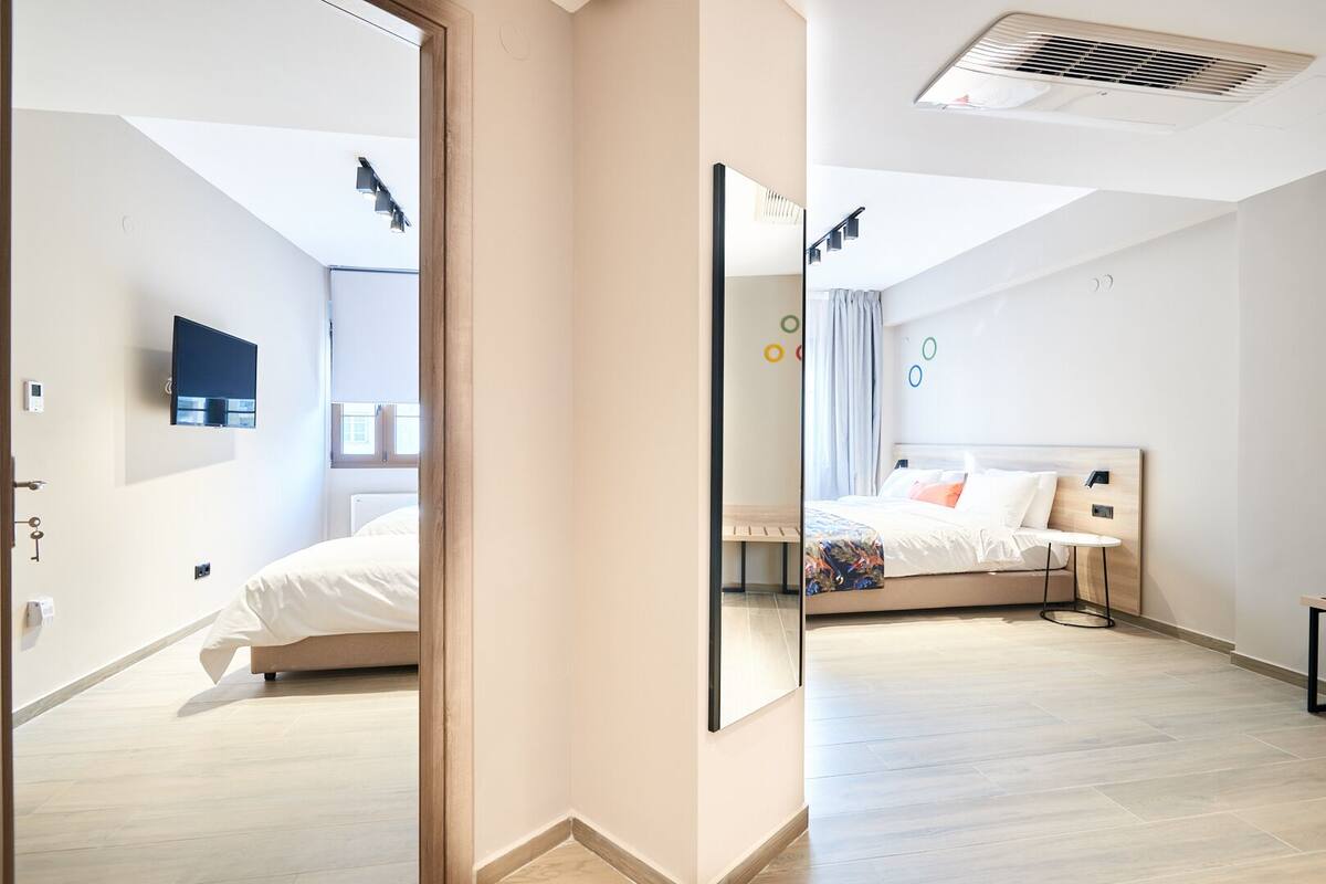 A modern hotel room with a bed, a bedside table, a TV mounted on the wall, and a ceiling vent.