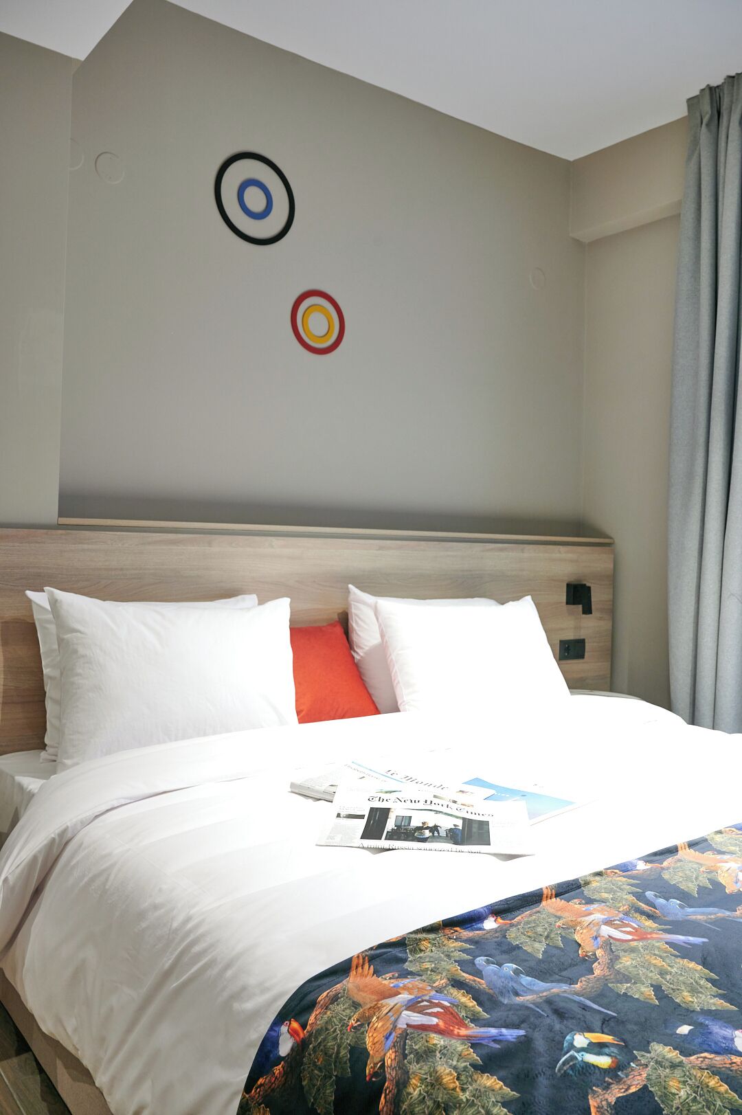 A hotel room with a neatly made bed, a target decoration on the wall, and a window with curtains.