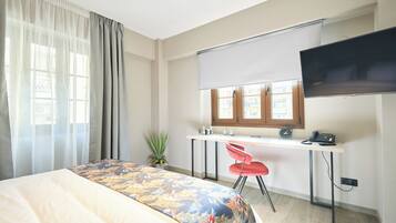 Une chambre d’hôtel avec un lit, un bureau avec un ordinateur, une télévision et une fenêtre avec des rideaux.