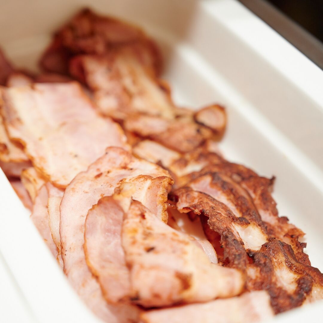 Una bandeja con carne cortada y cocida, probablemente jamón o tocino, en un recipiente blanco.