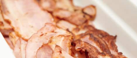 A tray of sliced cooked meat, likely ham or bacon, in a white container.