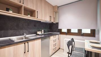 A modern kitchen with wooden cabinets, a black countertop, a built-in dishwasher, and a dining area with a table and chairs.