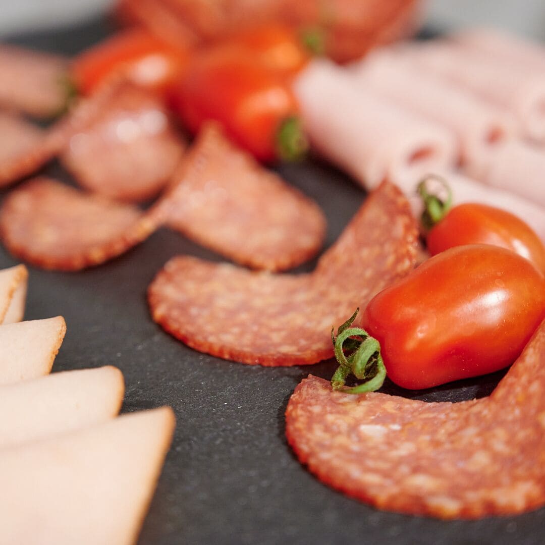 Diversidad de embutidos curados y lonchas de queso sobre una tabla de piedra pizarra.