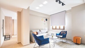 Un salon moderne avec un canapé, deux fauteuils bleus, une table basse et un petit meuble orange.