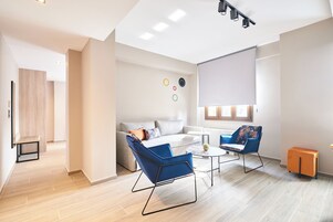 Ein modernes Wohnzimmer mit einer Couch, zwei blauen Sessel, einem Couchtisch und einem kleinen, orangefarbenen Schrank.