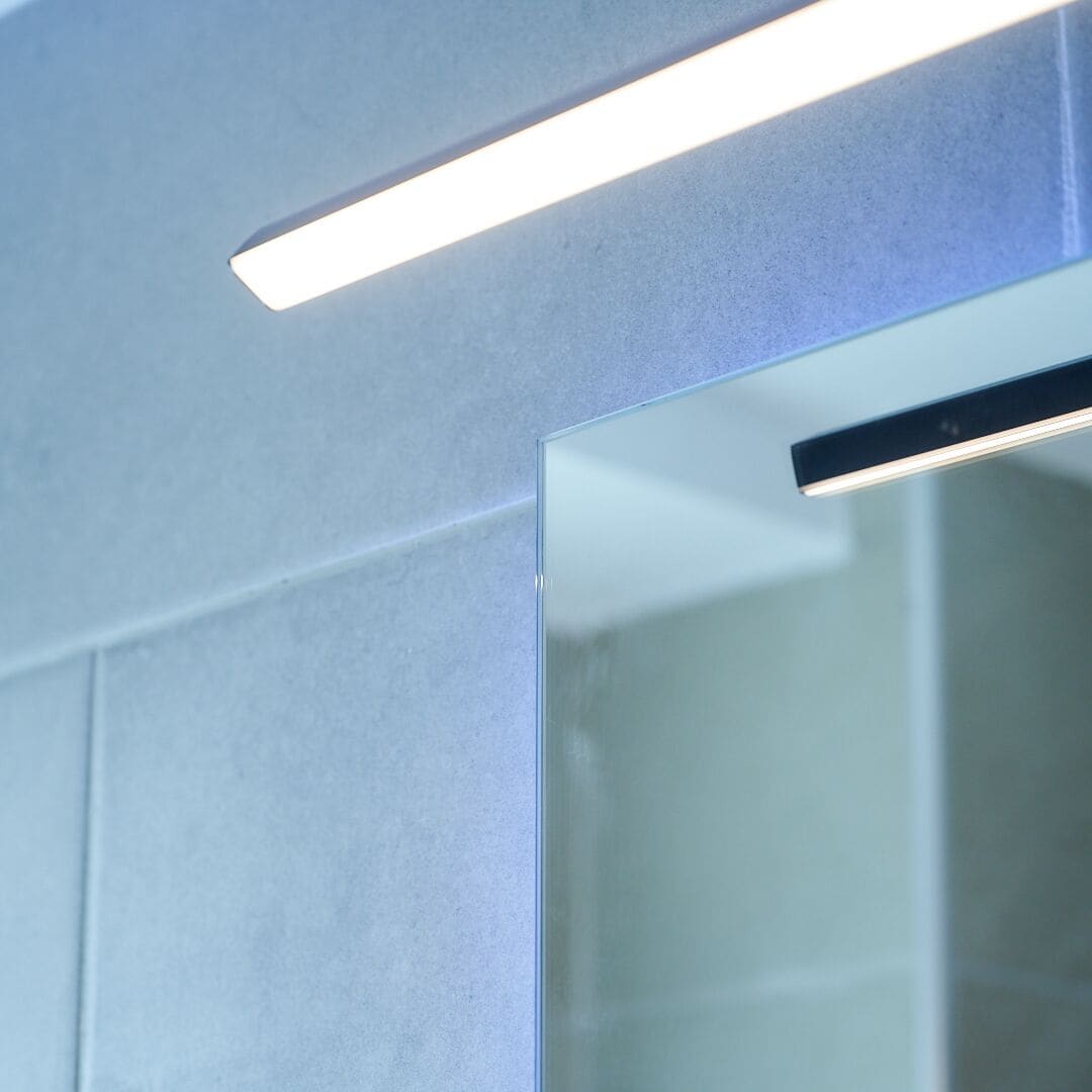 A modern bathroom with a glass shower enclosure and a linear light fixture.