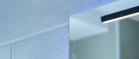 A modern bathroom with a glass shower enclosure and a linear light fixture.