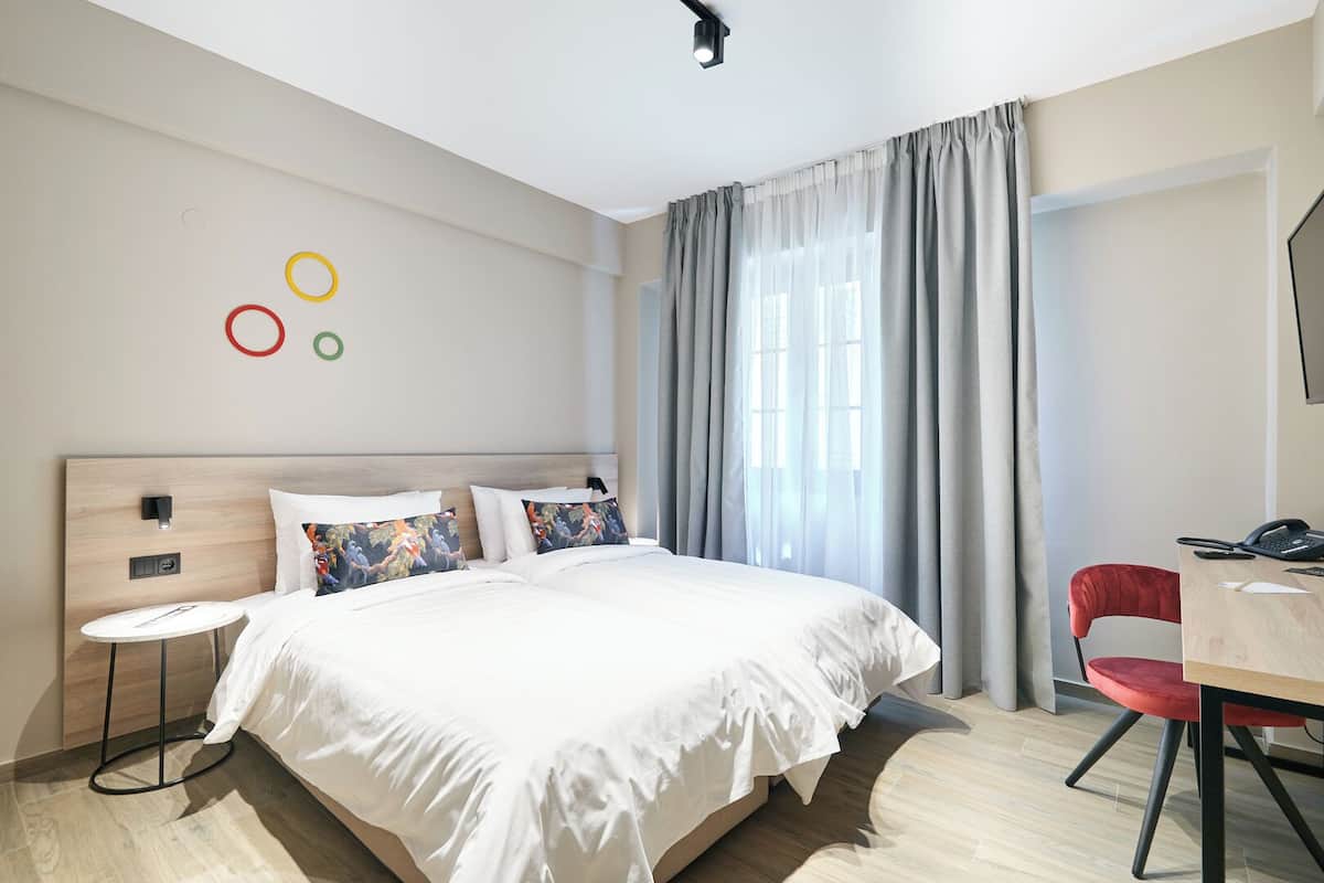 A hotel room with a large bed, a desk with a chair, a TV, and a window with curtains.