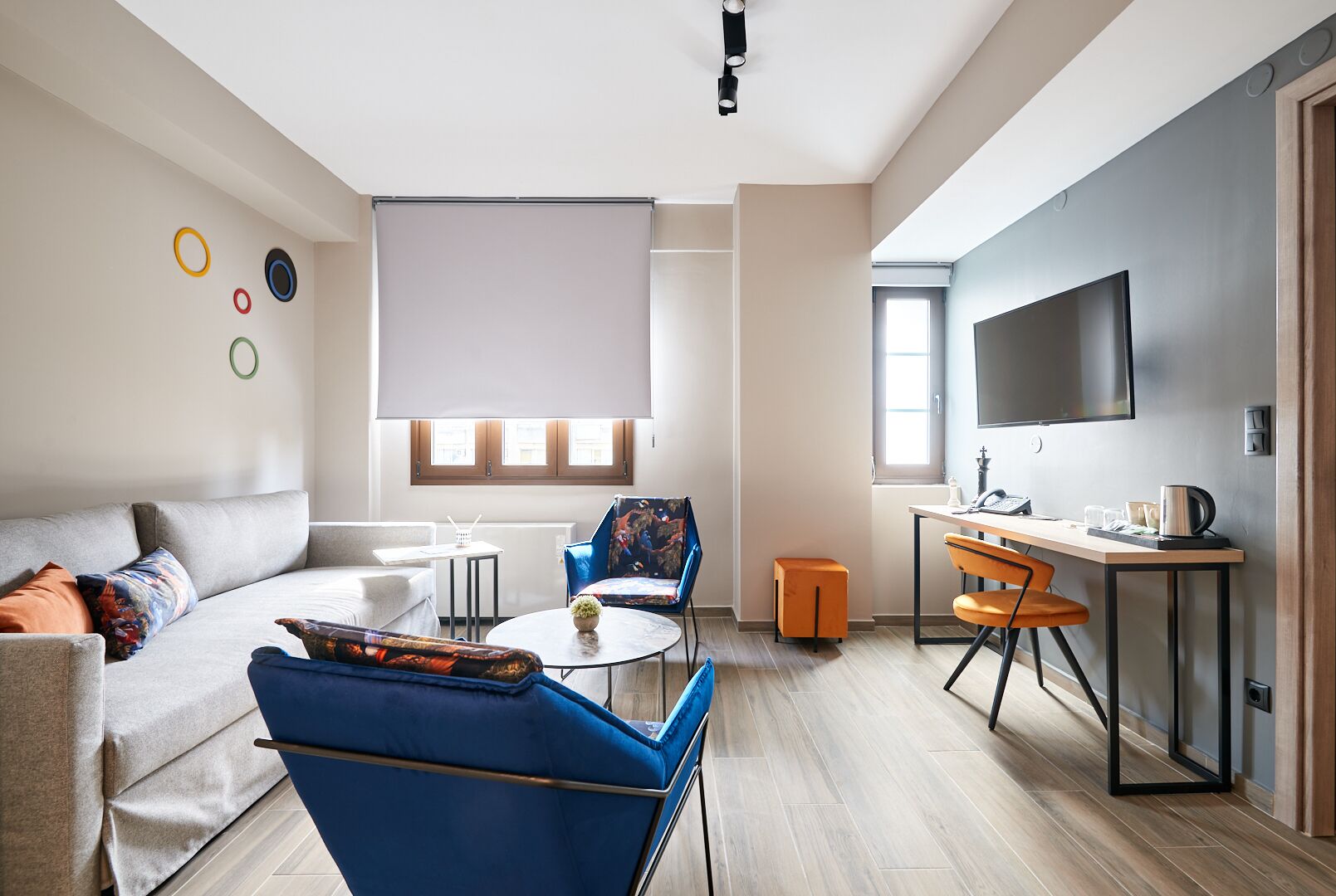 A modern living room with a sofa, a blue armchair, a small round table, and a TV mounted on the wall.