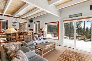 Amplia sala de estar con un sofá grande, una mesa de centro y una chimenea. Grandes ventanas ofrecen vistas al exterior.