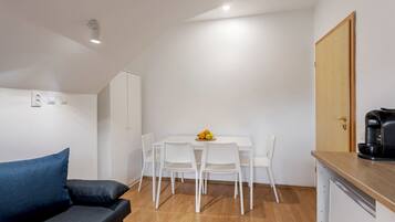 A compact living space with a sofa, a dining table with chairs, a coffee machine, and a wardrobe.