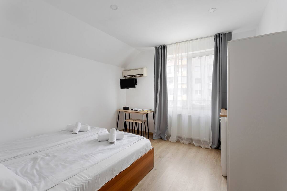 A modern hotel room with a single bed, a desk, and a large window with curtains.
