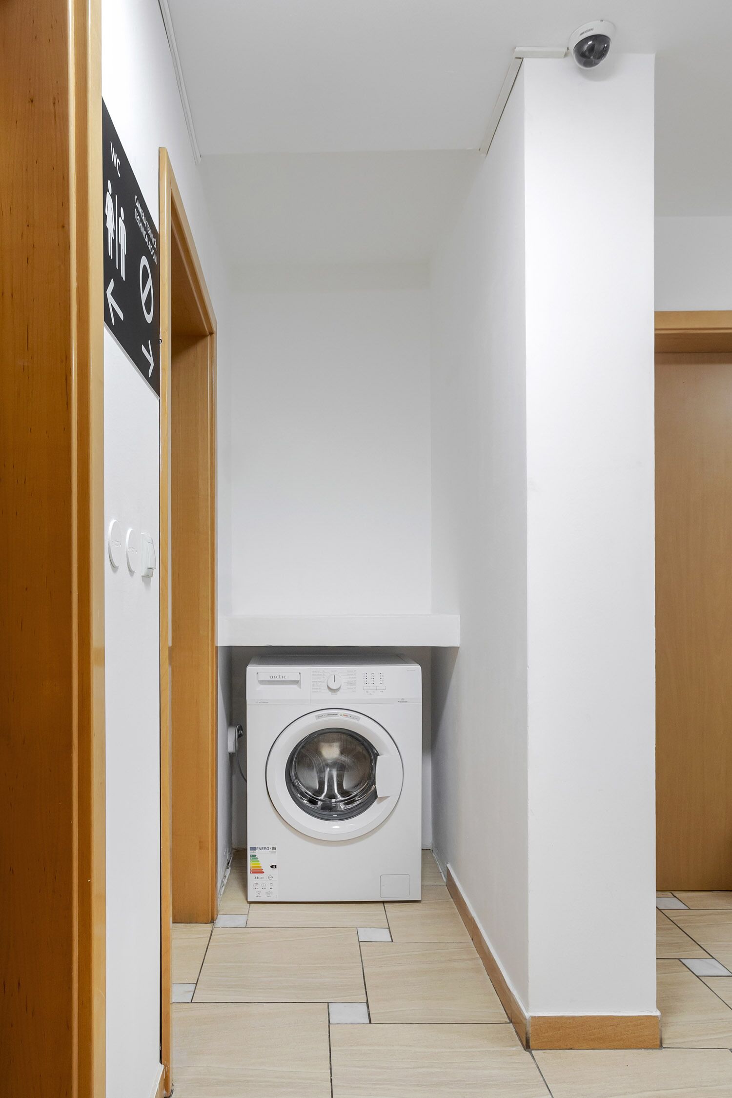 A laundry room with a front-loading washing machine, a wooden door, and a white wall.