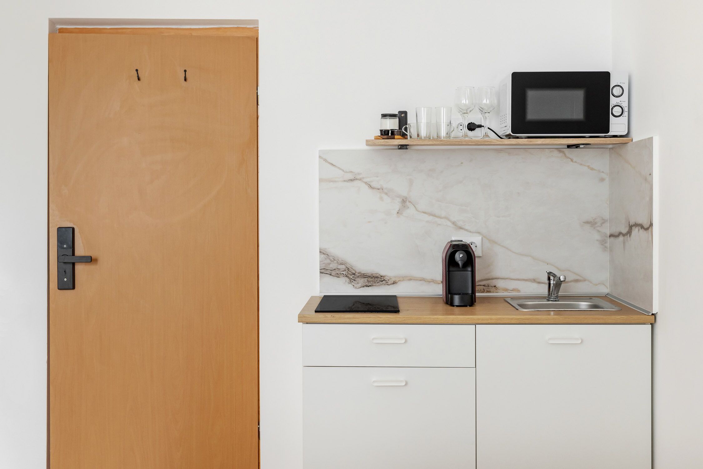 Una cocina compacta con microondas, cafetera y un lavamanos pequeño.
