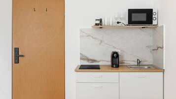 Una cocina compacta con microondas, cafetera y un lavamanos pequeño.