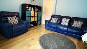 Een woonkamer met twee blauwe leren banken, een zwarte opbergkast en een grijze vloerkleed.