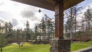 A stone pillar with a metal grill, a stone wall, and a view of a grassy area with trees and a body of water. - Newly Listed! Cabin-style home. (TFH) (Friday Harbor)