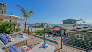 A rooftop pool area with lounge chairs, a hot tub, and a view of the ocean.