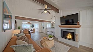 A spacious living room with a fireplace, a television mounted above it, and a ceiling fan.
