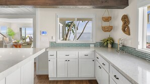 A modern kitchen with white cabinets, a large window with a view, and a hanging basket.