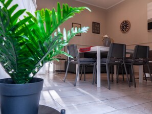 A dining area with a table and chairs, a potted plant, and a wall clock.