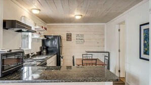 A compact kitchen with a microwave, stove, and sink, a dining area with a table and chairs, and a framed artwork on the wall. - Merry Macaw (Rockport)