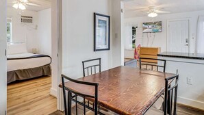 A room with a wooden dining table, four chairs, a bed, and a kitchenette. - Merry Macaw (Rockport)