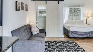 A room with a gray sofa, a bed with a white headboard, a black and white patterned rug, and a white door. - Merry Macaw (Rockport)