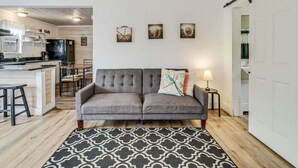 A living room with a grey sofa, a patterned rug, and three wall-mounted pictures. - Merry Macaw (Rockport)