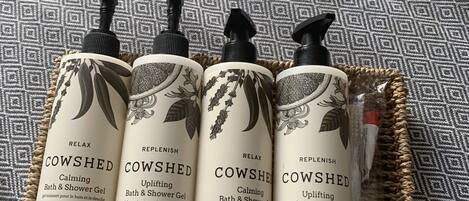 Four bottles of Cowshed Bath & Shower Gel on a woven tray.