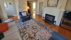 Un salon avec un fauteuil bleu, un tapis à motifs, une cheminée et un téléviseur.