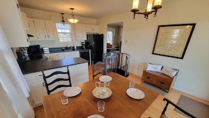 Une cuisine moderne avec des meubles blancs, un réfrigérateur noir et un coin repas comprenant une table et des chaises en bois.