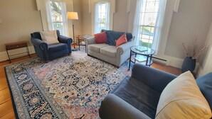 Un salon avec un canapé bleu, un canapé gris, un tapis à motifs et une petite table ronde.