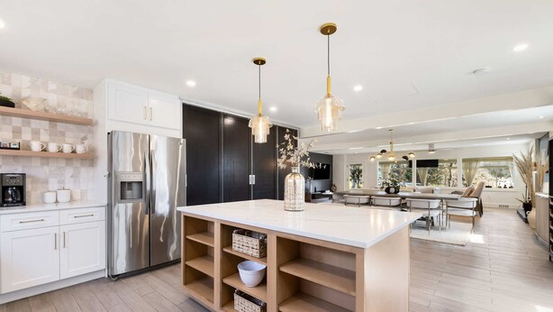 Eine moderne Küche mit weißen Schränken, einem Edelstahl-Kühlschrank, Holzregalen und Pendelleuchten.