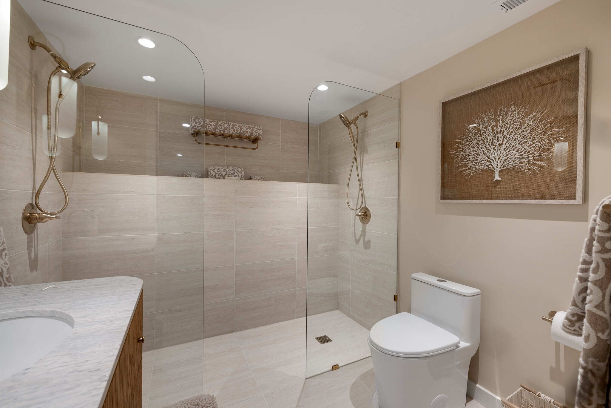 Un baño moderno con ducha envuelta en vidrio, lavamanos de mármol y un inodoro.