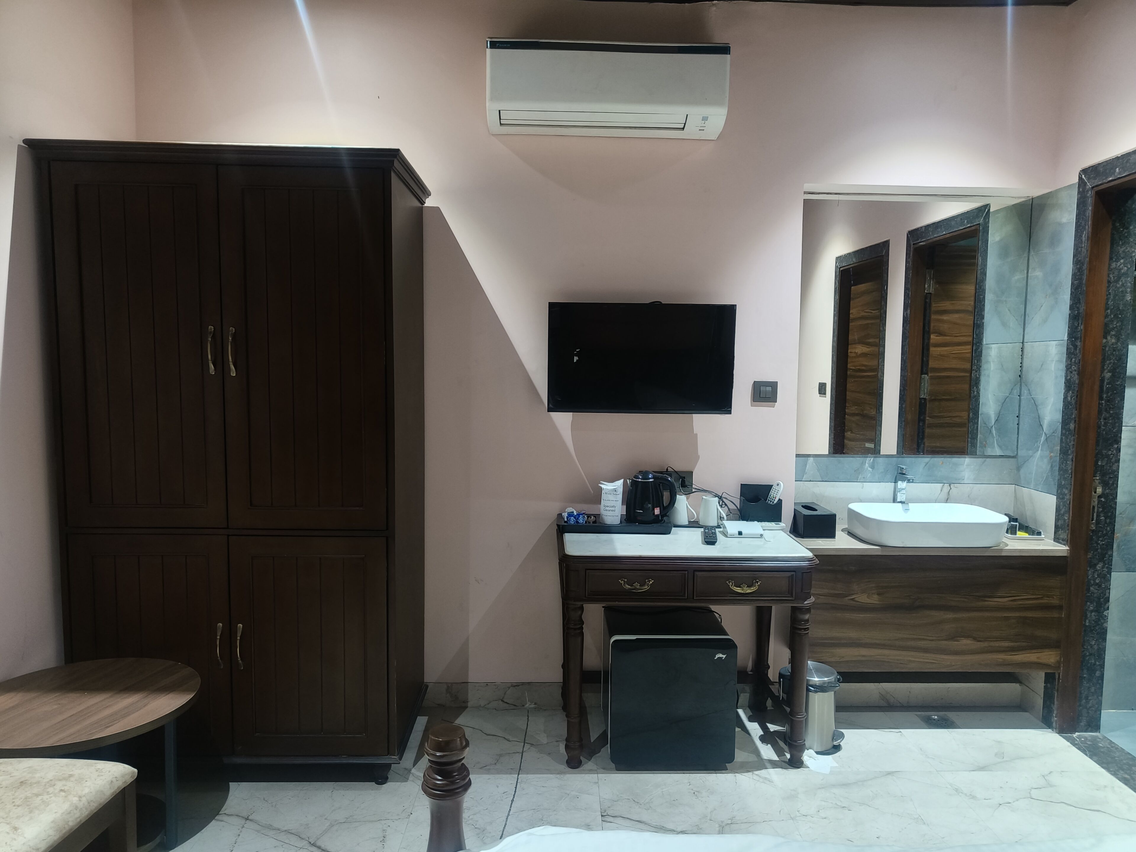 A bathroom with a wooden wardrobe, a desk with a flat-screen TV, a sink, and a mirror.