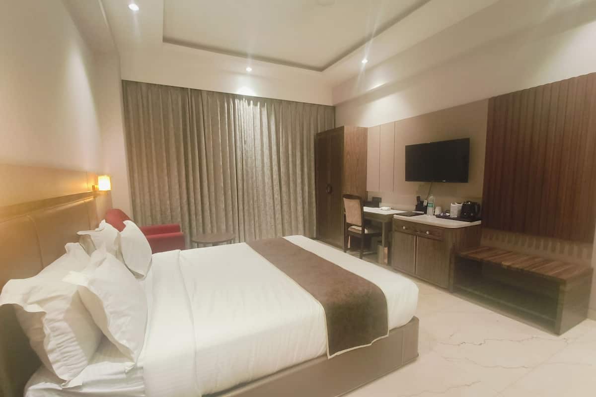 Une chambre d’hôtel avec un grand lit, un bureau avec une chaise, une télévision et un coin salon avec un banc.