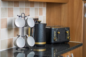 Een keuken met een zwarte en gouden toaster, een waterkoker en een muggenrek met vier mokken.
