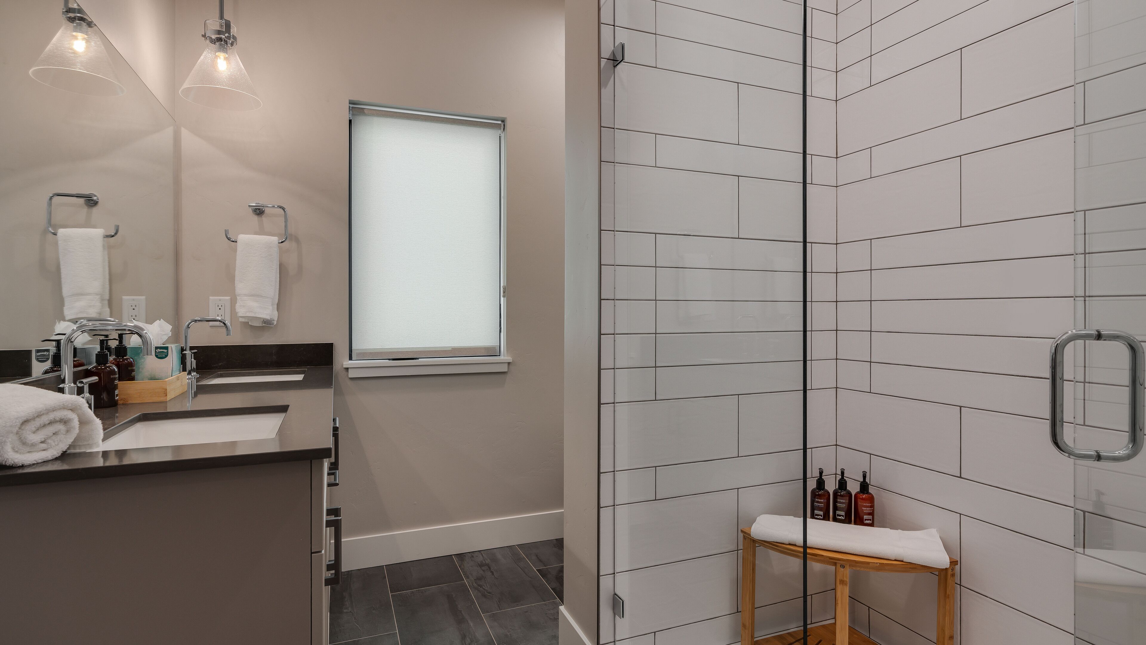 A modern bathroom with a glass shower enclosure, a vanity with a mirror, and a window.