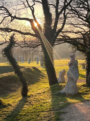 A serene park with stone statues, a grassy area, and a tree with sunlight streaming through.