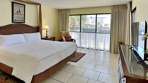 Hotelkamer met een groot bed, een bureau met televisie, een stoel, een raam met gordijnen en een ingelijst schilderij aan de muur.