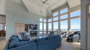 Een ruime woonkamer met een grote blauwe bank, een open haard en uitzicht op het strand.