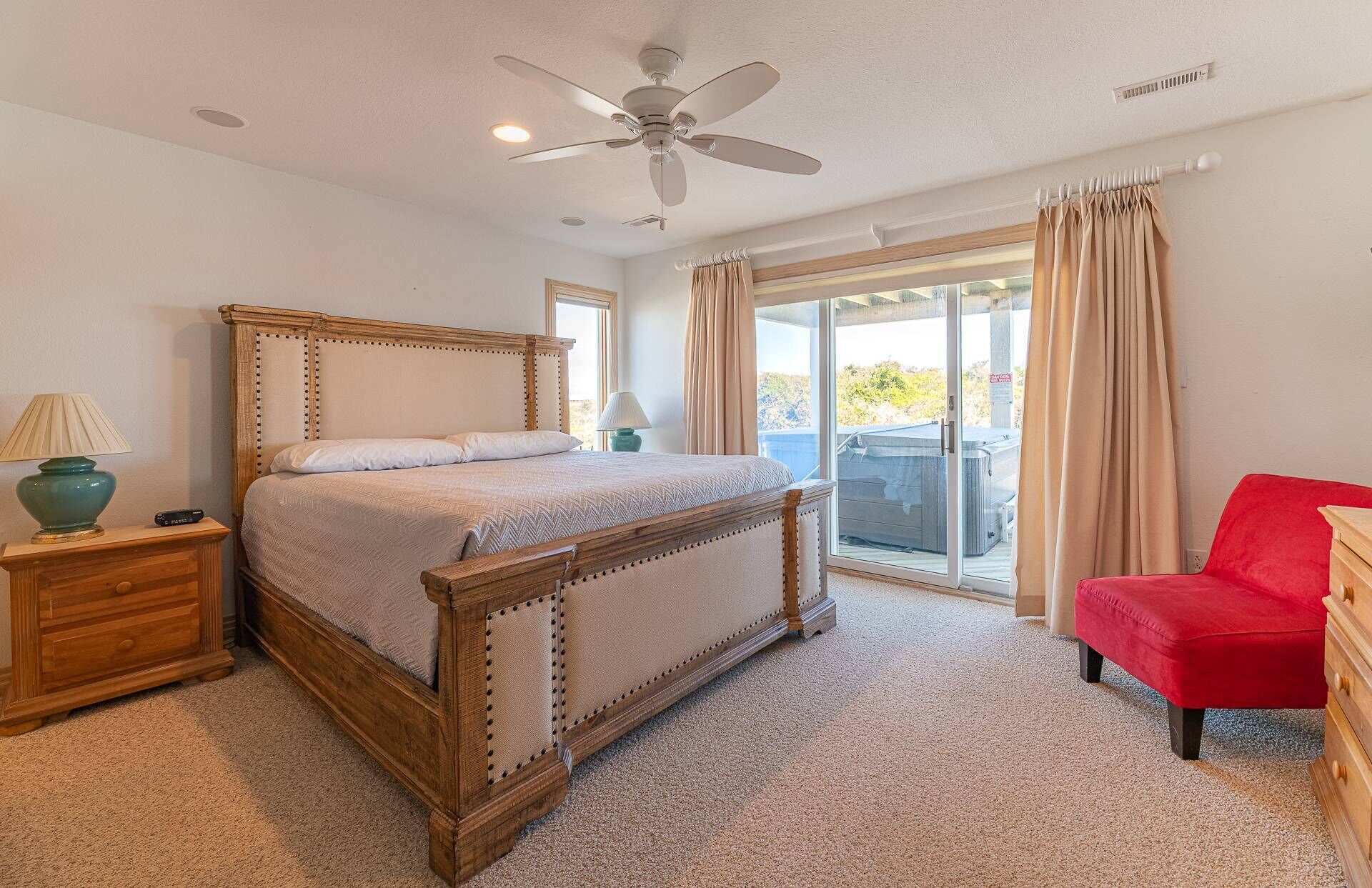 A bedroom with a wooden bed, a nightstand, a red chair, and a view of the outdoors through a sliding glass door.