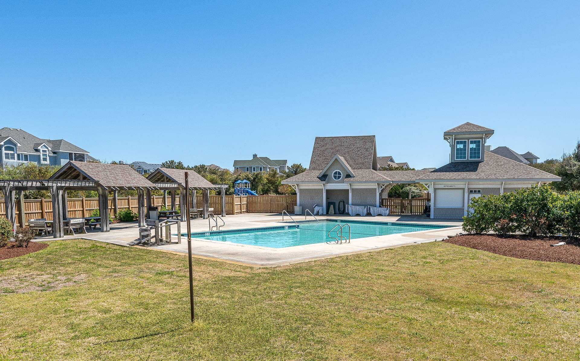 A residential area with a swimming pool, wooden gazebos, and a house with a garage.