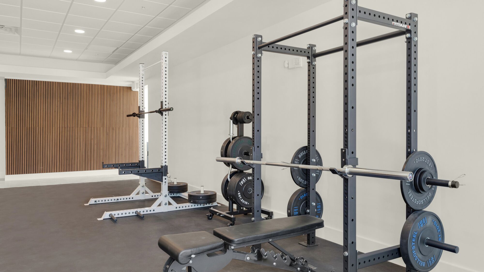 A gym with weightlifting equipment, a bench, and a wooden panel wall.