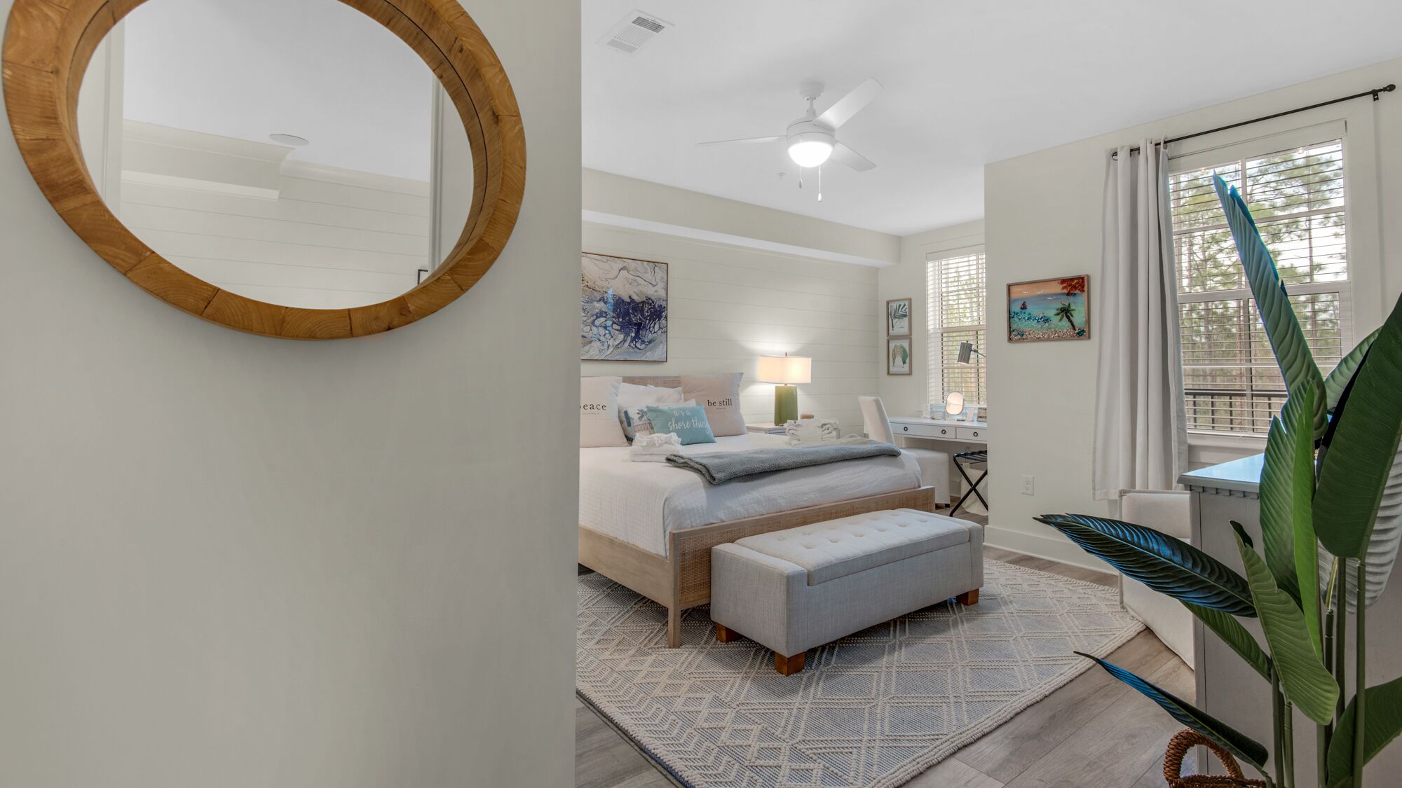 A bedroom with a bed, bedside table, lamp, desk, chair, and a large mirror.
